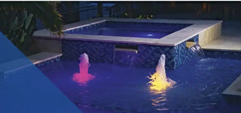 Night-time pool scene illuminated by two ColorVision® LED Bubblers, one emitting pink and the other yellow light. Both lights are shooting water up to a foot in the air.